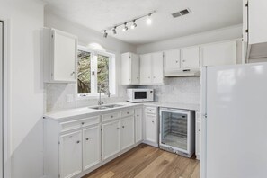A modern kitchen with white cabinetry, a built-in microwave, and a refrigerator. - Wavecrest Cottage-Sleeps 14 Beach (Laketown Township)