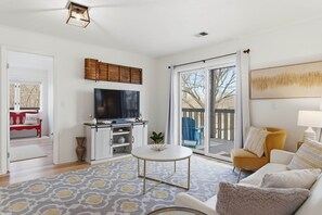 A living room with a television, a coffee table, and a sofa. There is a sliding glass door leading to an outdoor area. - Wavecrest Cottage-Sleeps 14 Beach (Laketown Township)