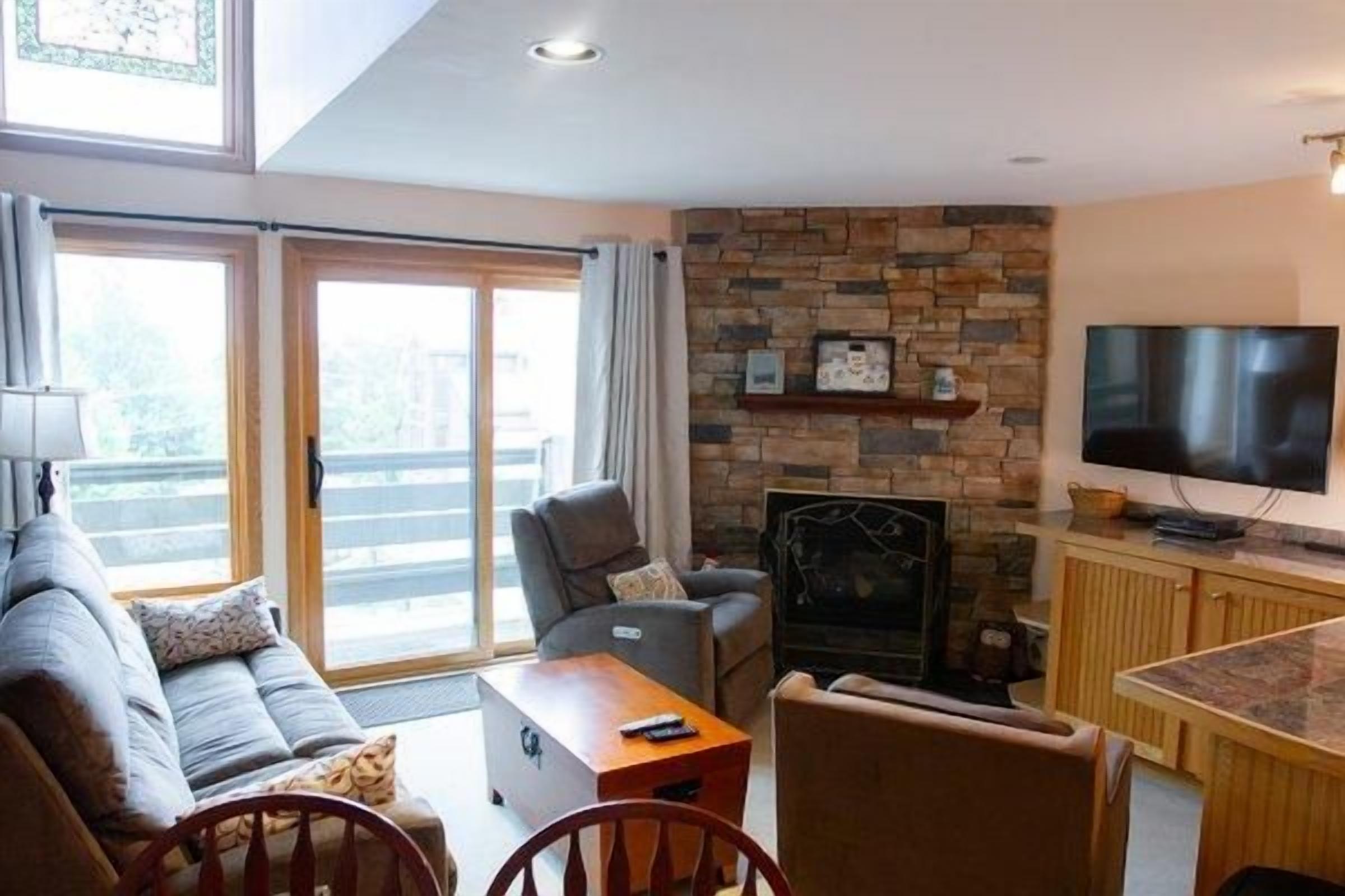 A living room with a sofa, chairs, a coffee table, a fireplace, a television, and a sliding glass door leading to an outdoor area.