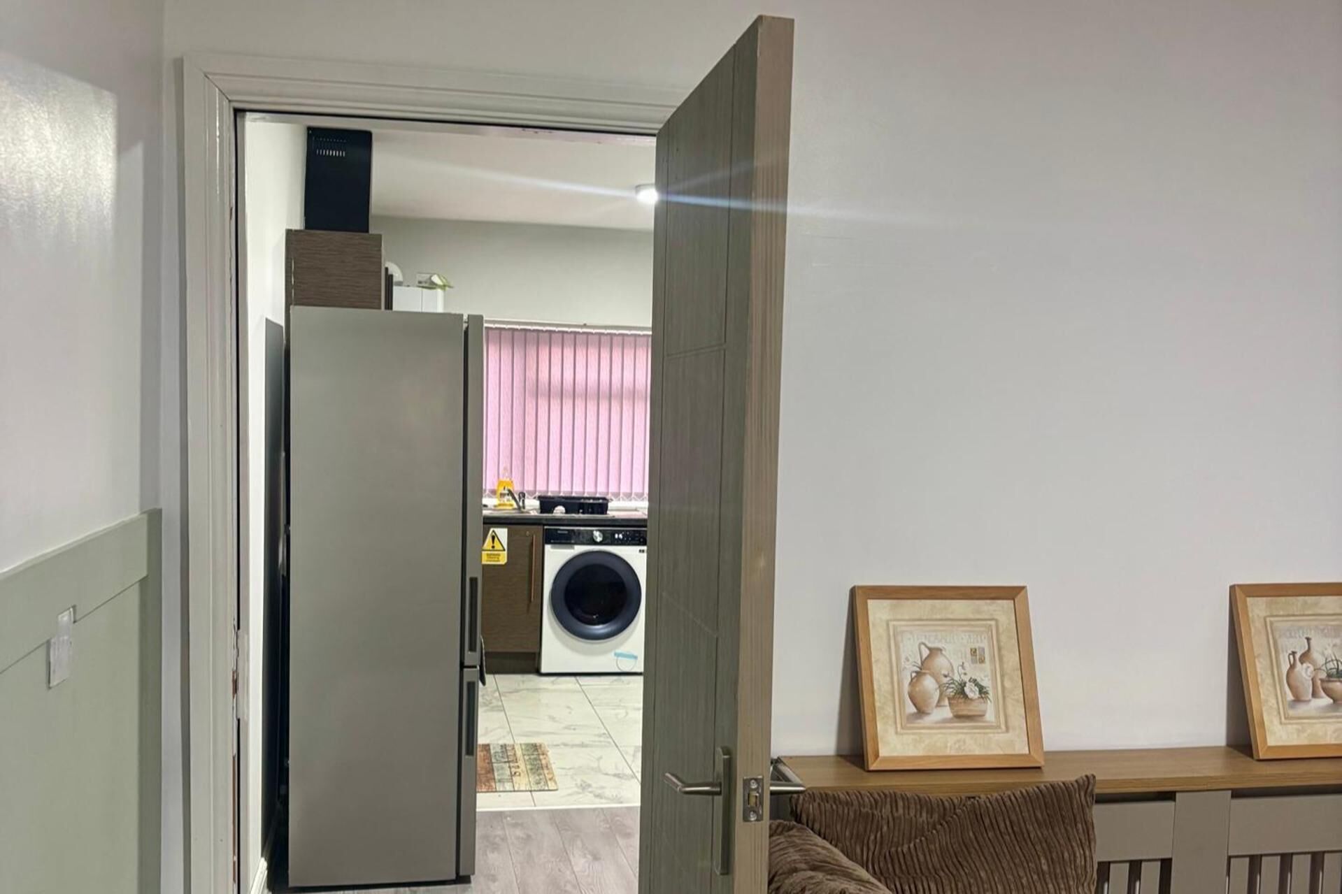 An open door leading to a laundry area with a washing machine and a dryer, a tiled floor, and a framed picture on a shelf.
