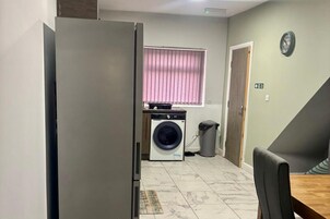 Cocina compacta con lavadora, un basurero y comedor con mesa y sillas.