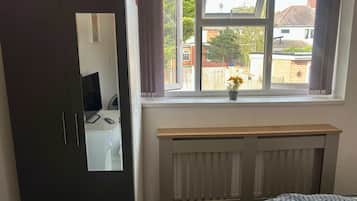Un dormitorio con cama, armario, radiador y ventana con vistas al exterior.
