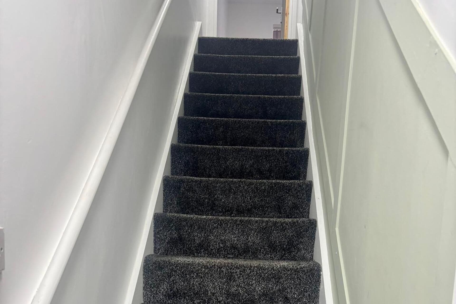 Eine Treppe mit dunklem Teppich und weißen Wänden.