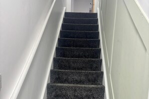 A staircase with dark carpeted steps and white walls.