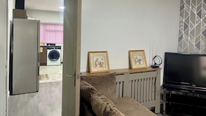 Una sala de estar con sofá, televisión y lavadora al fondo.