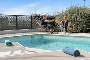 A swimming pool with lounge chairs and a table, surrounded by a fence and vegetation. - Vila Helios in Pomer by Istrabook (Pomer)