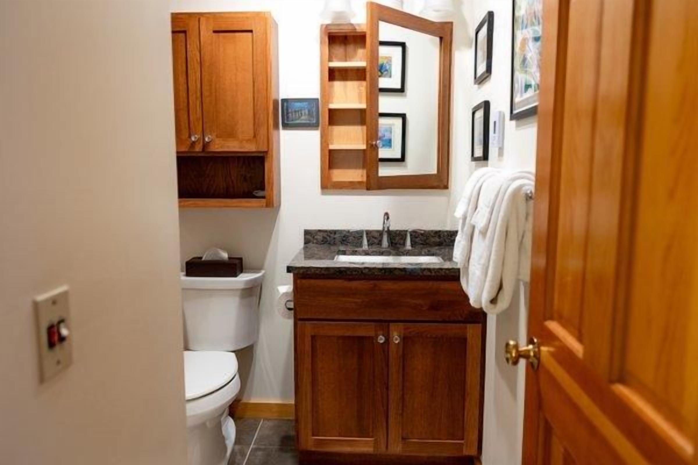 A compact bathroom with a toilet, wooden cabinets, a sink, and a mirror.