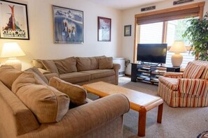 Een woonkamer met een bank, fauteuil, salontafel, televisie en een plant.
