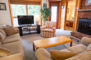 Een woonkamer met een bank, fauteuils, een salontafel, een tv op een dressoir en een open haard.