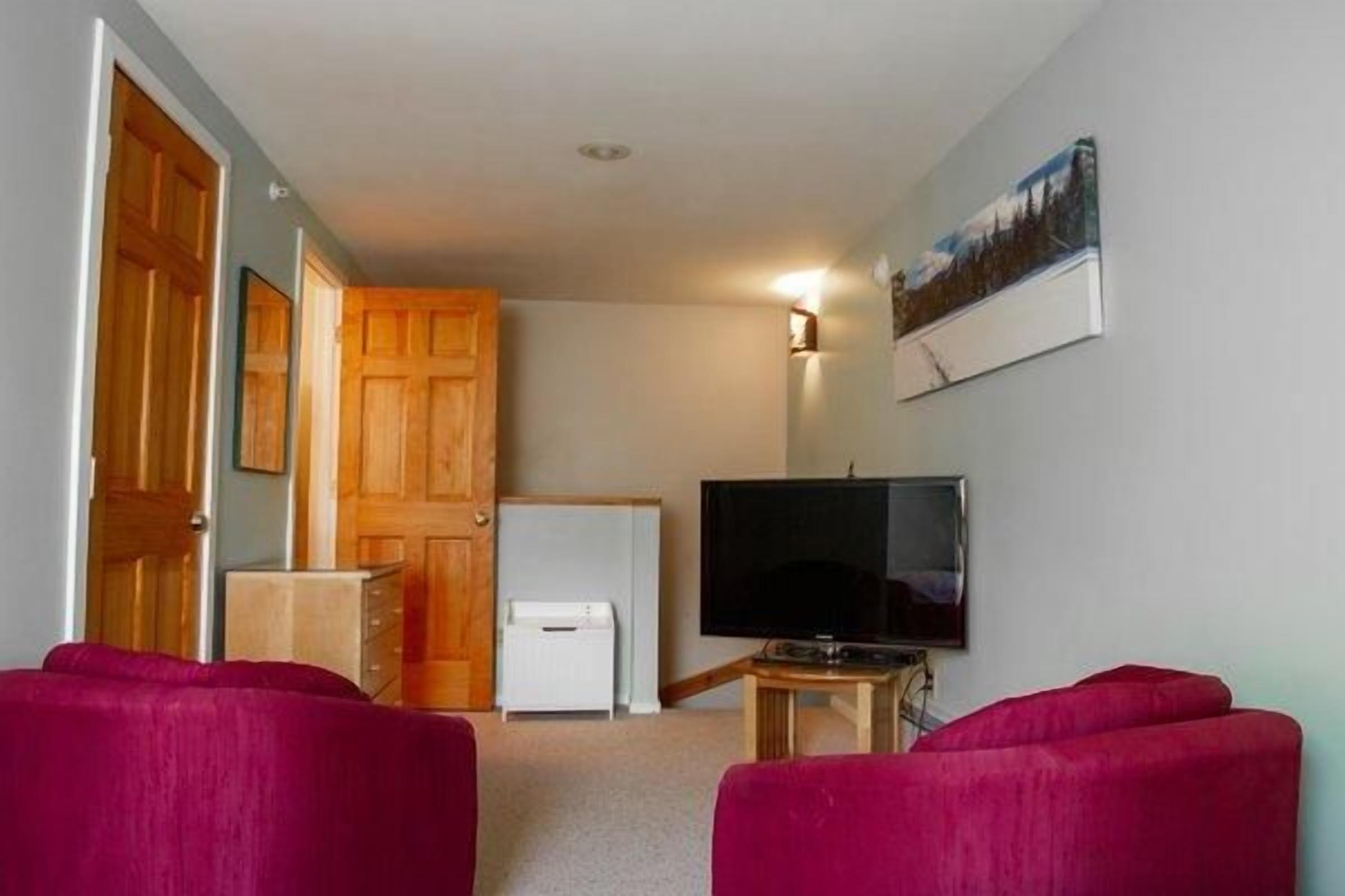 Et værelse med fjernsyn, en dør, et hvidt skab og en rød sofa.