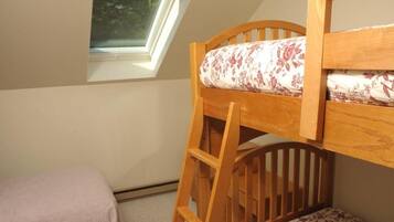 Una cama litera con escalera de madera, una ventana con vistas a la vegetación y una mesita de noche con un cojín estampado con motivos florales.