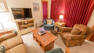 Una sala de estar con televisor, sofá, sillón, mesa de centro y cortina roja.