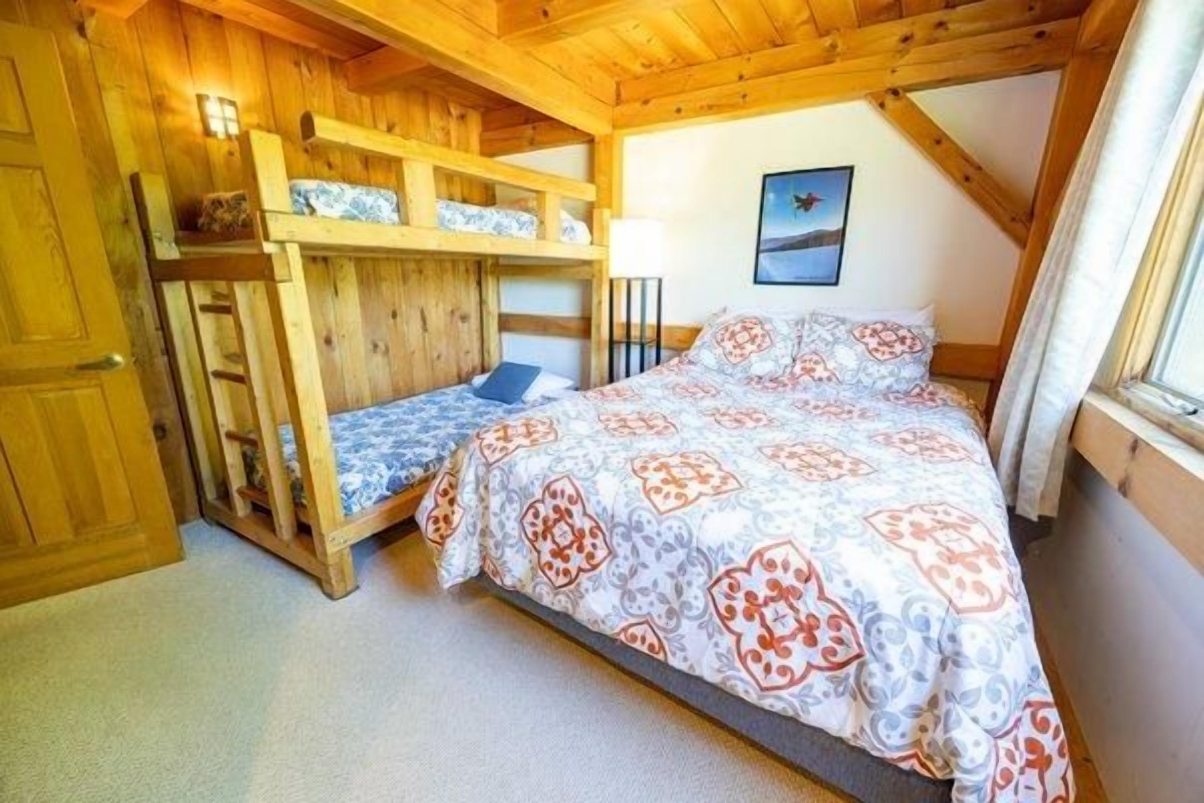 A room with bunk beds, a single bed, a framed picture on the wall, and a window with curtains.