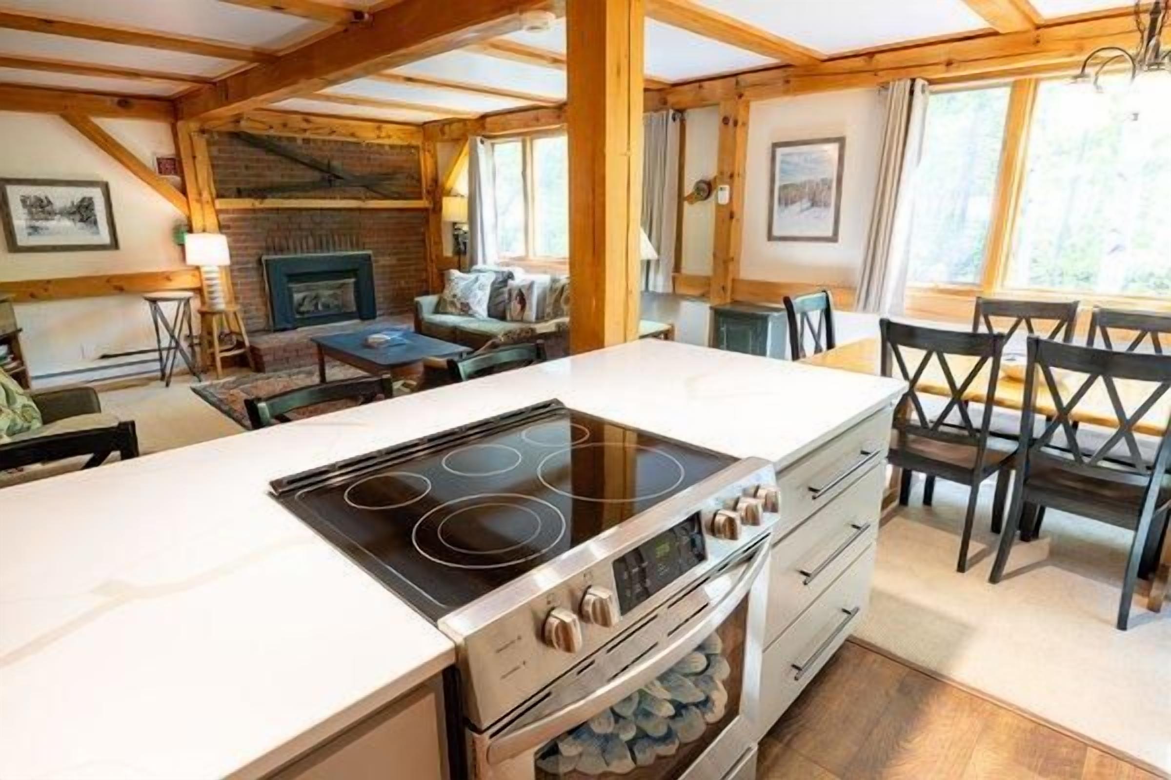 A kitchen with a central island, wooden ceiling beams, and a dining area with chairs.