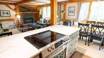 A kitchen with a central island, wooden ceiling beams, and a dining area with chairs.
