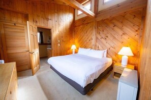 A wooden-paneled bedroom with a bed, two bedside lamps, and a door leading to another room. - Sugarloaf Mountain Birchwood III  C729 (Carrabassett Vly)