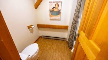 A small bathroom with a wooden floor, a white toilet, a wooden bench, and a poster on the wall.