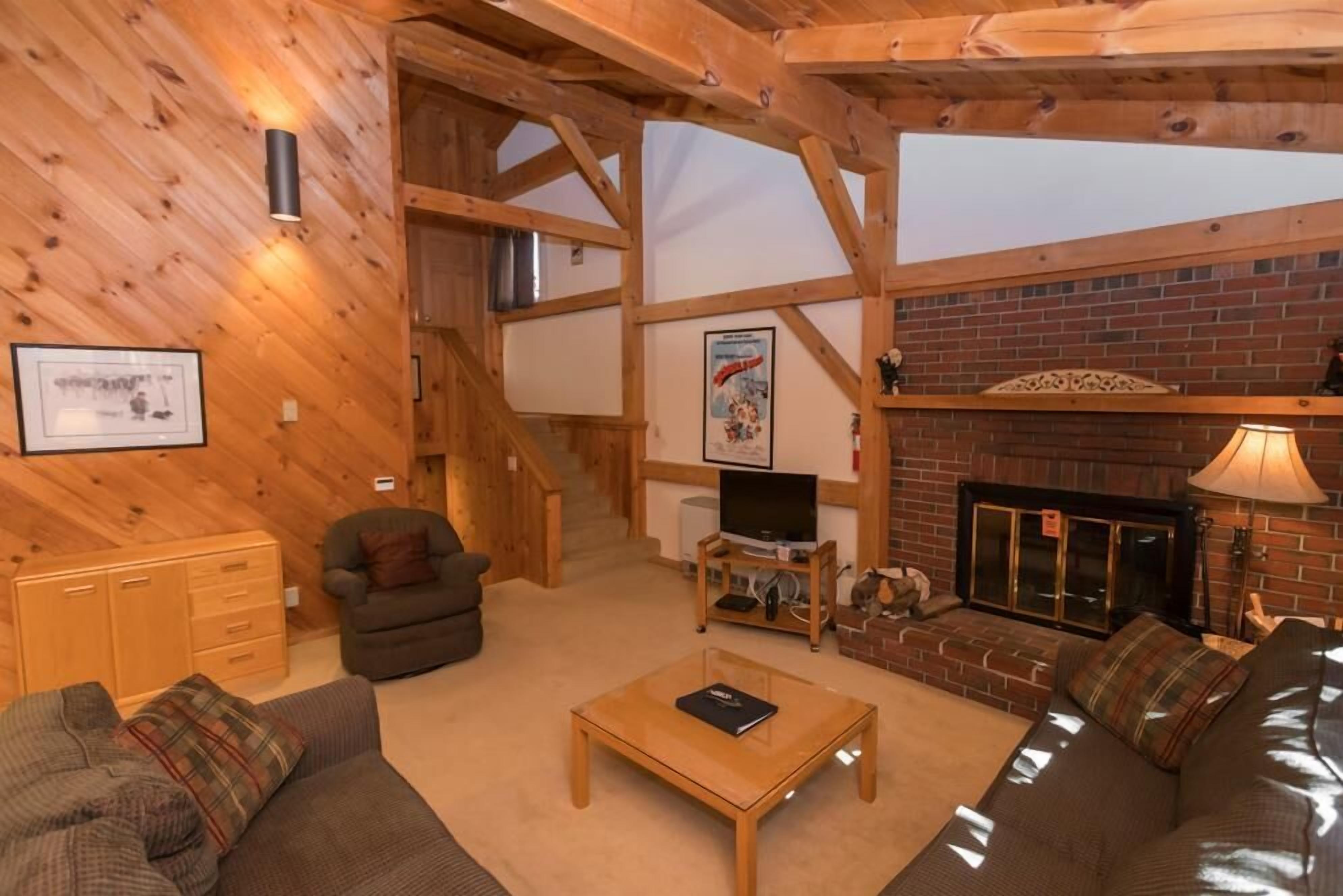 A cozy living room with a fireplace, wooden beams, a television, and a staircase.