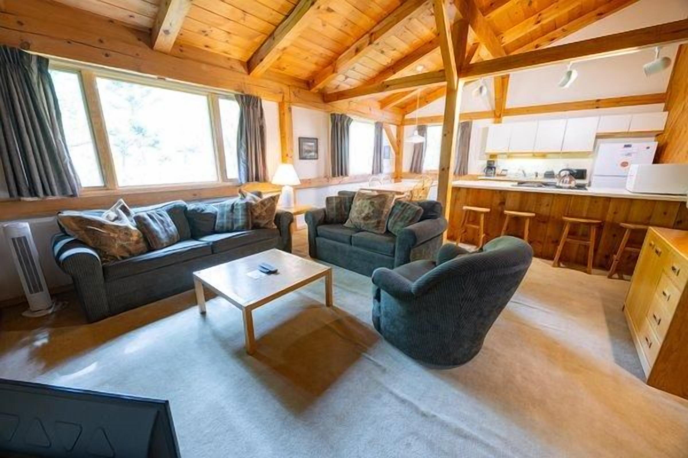 Hyggelig indretning med sofa, lænestol og et lille bord i et rum med synlige træbjælker.