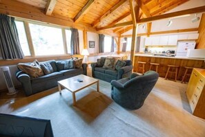 Un intérieur chaleureux avec un canapé, un fauteuil et une petite table dans une pièce aux poutres apparentes.