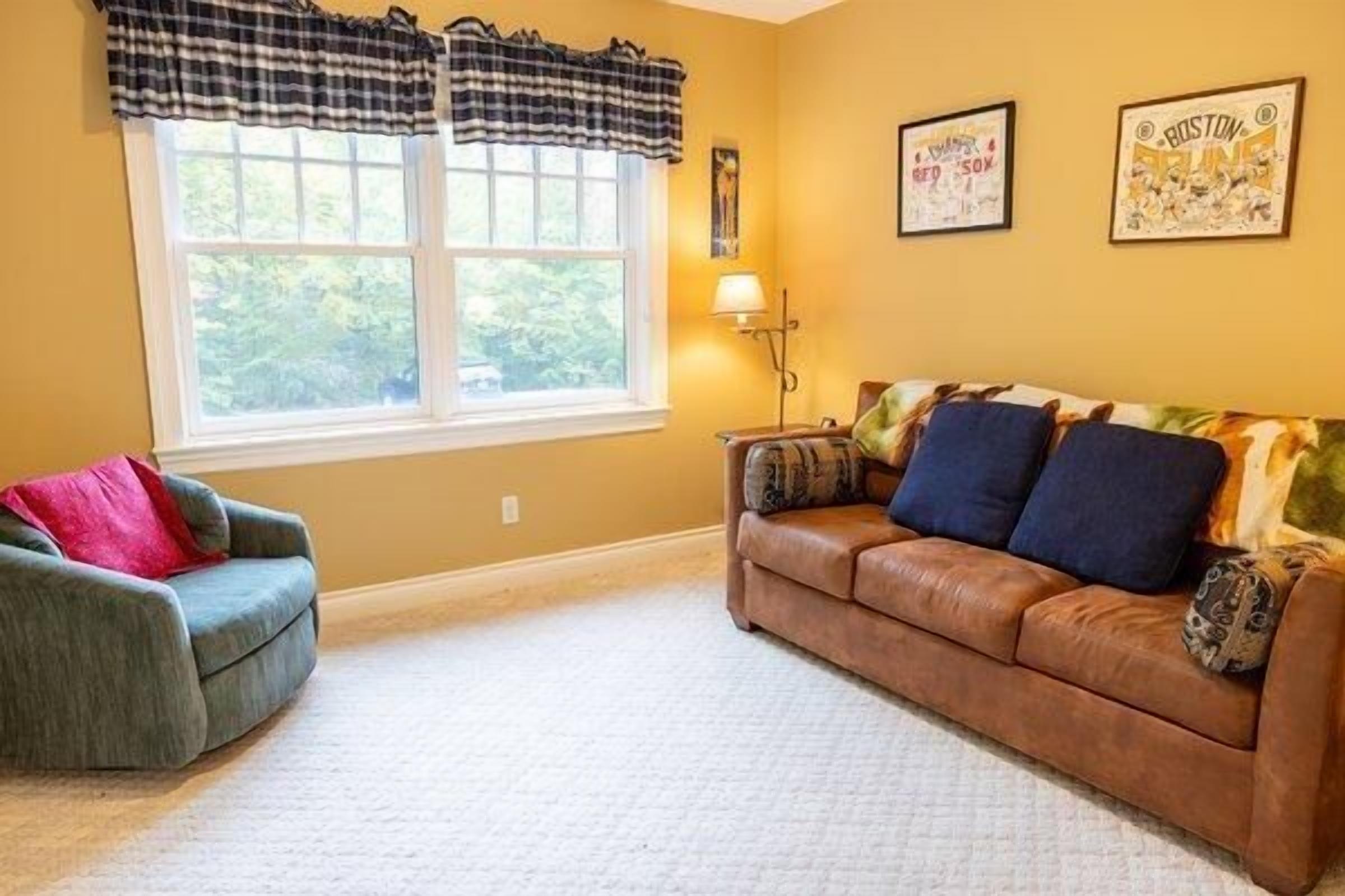 A living room with a brown leather sofa, a blue armchair, and a window with curtains.