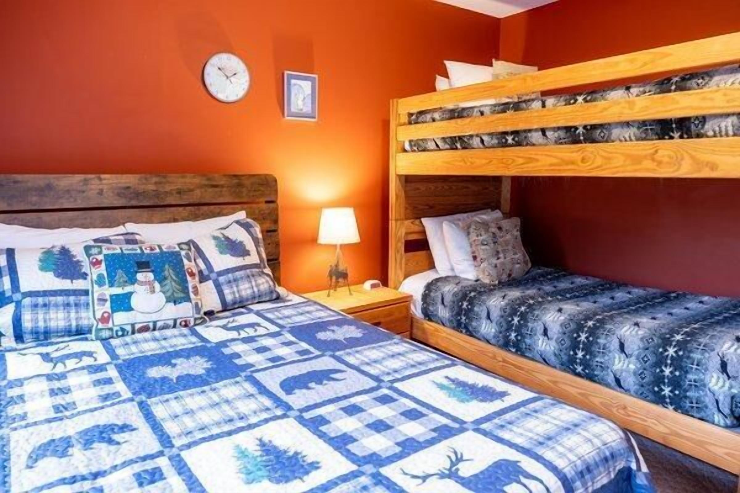 Une chambre avec un lit superposé, un lit simple avec une couverture bleue et une table de chevet avec une lampe.