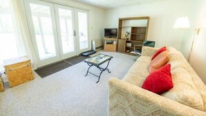 Una sala de estar con un sofá, televisor, mesa de centro y puerta corrediza de vidrio que da a un área exterior.