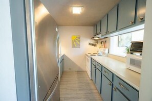 A narrow kitchen with light blue cabinets, a stainless steel refrigerator, and a microwave on the counter. - Sugarloaf Mountain Kibby Mountain Road C2318 (Carrabassett Vly)