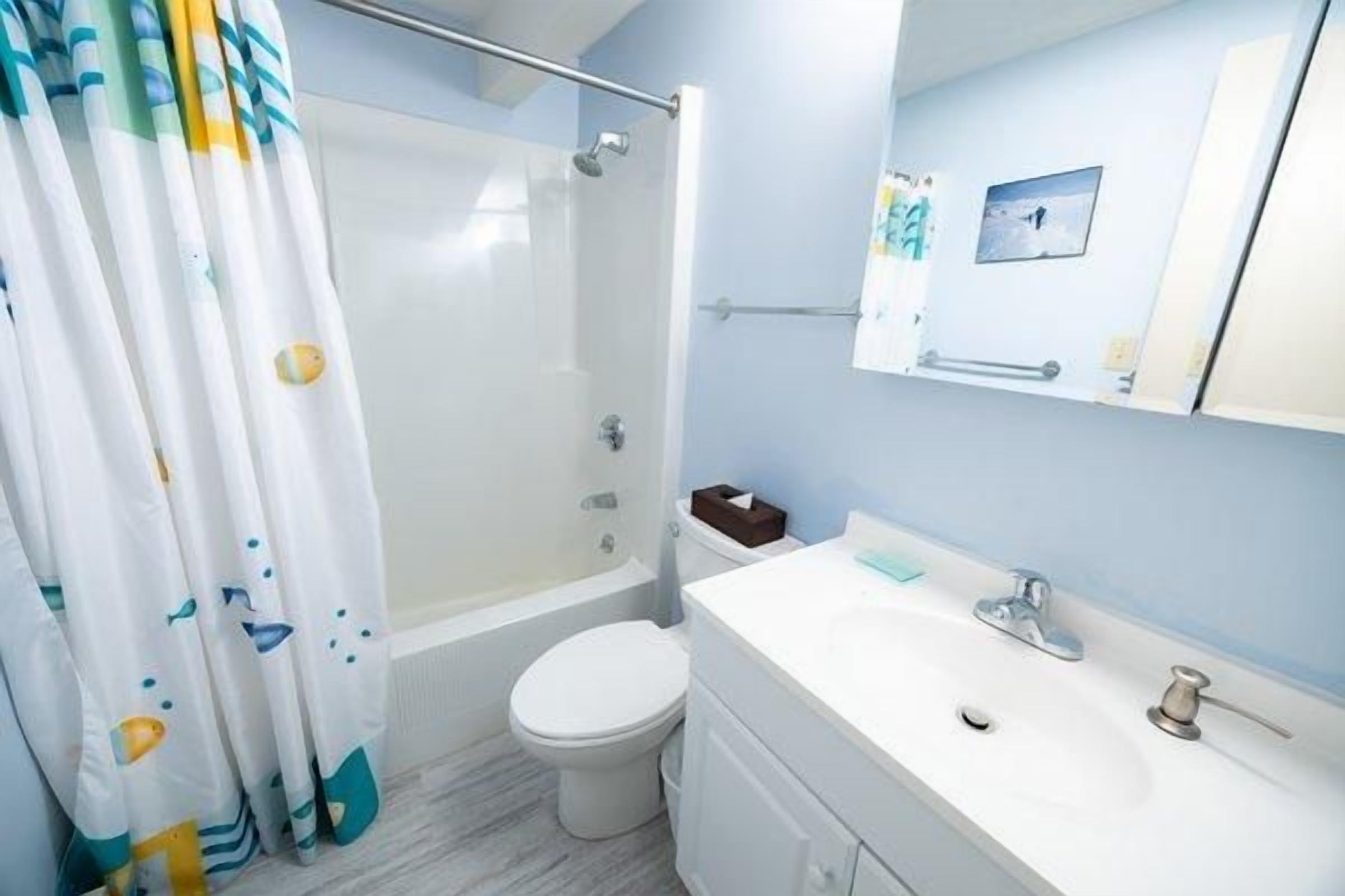 A bathroom with a shower, toilet, sink, and a mirror.