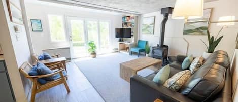 Amplia sala de estar con sofá, mesa de centro y chimenea. Hay un televisor y una estantería en la habitación.