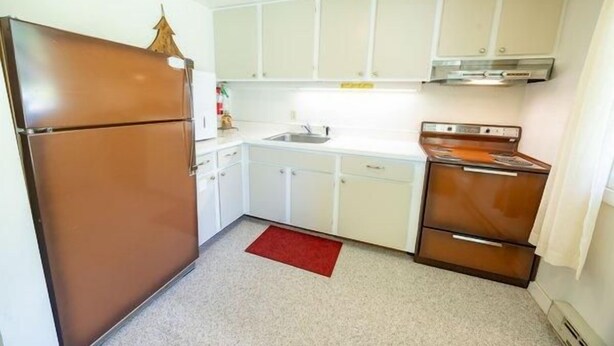 Cocina compacta con refrigerador, estufa y armarios blancos.