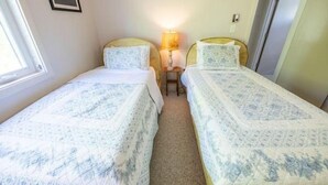 Un dormitorio pequeño y bien iluminado con dos camas individuales, una mesita de noche con lámpara y un cuadro en la pared.