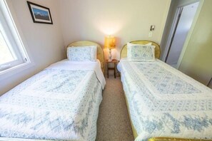 Ein kleines, helles Schlafzimmer mit zwei Einzelbetten, einem Nachttisch mit Lampe und einem gerahmten Bild an der Wand.