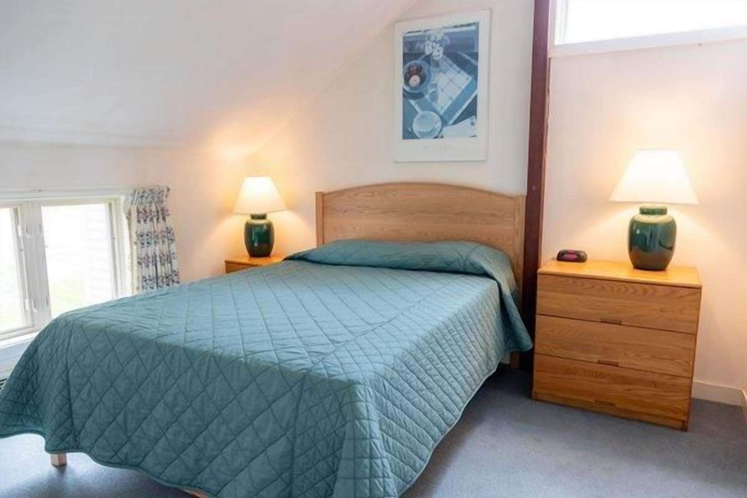 A bedroom with a bed, two bedside tables, a nightstand, and a window with curtains.