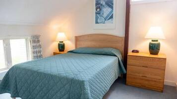 A bedroom with a bed, two bedside tables, a nightstand, and a window with curtains.
