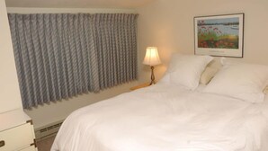 Una camera d'albergo con un letto, una lampada, una finestra con tende e un quadro appeso al muro.