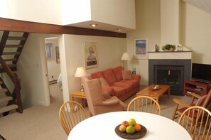 A living room with a sofa, a table with fruit, a fireplace, and a television. - Sugarloaf Mountain Kibby Mountain Road C2315 (Carrabassett Vly)