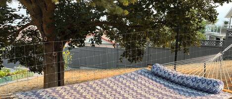 A hammock set up on a patterned mat outdoors, surrounded by trees and a fence.