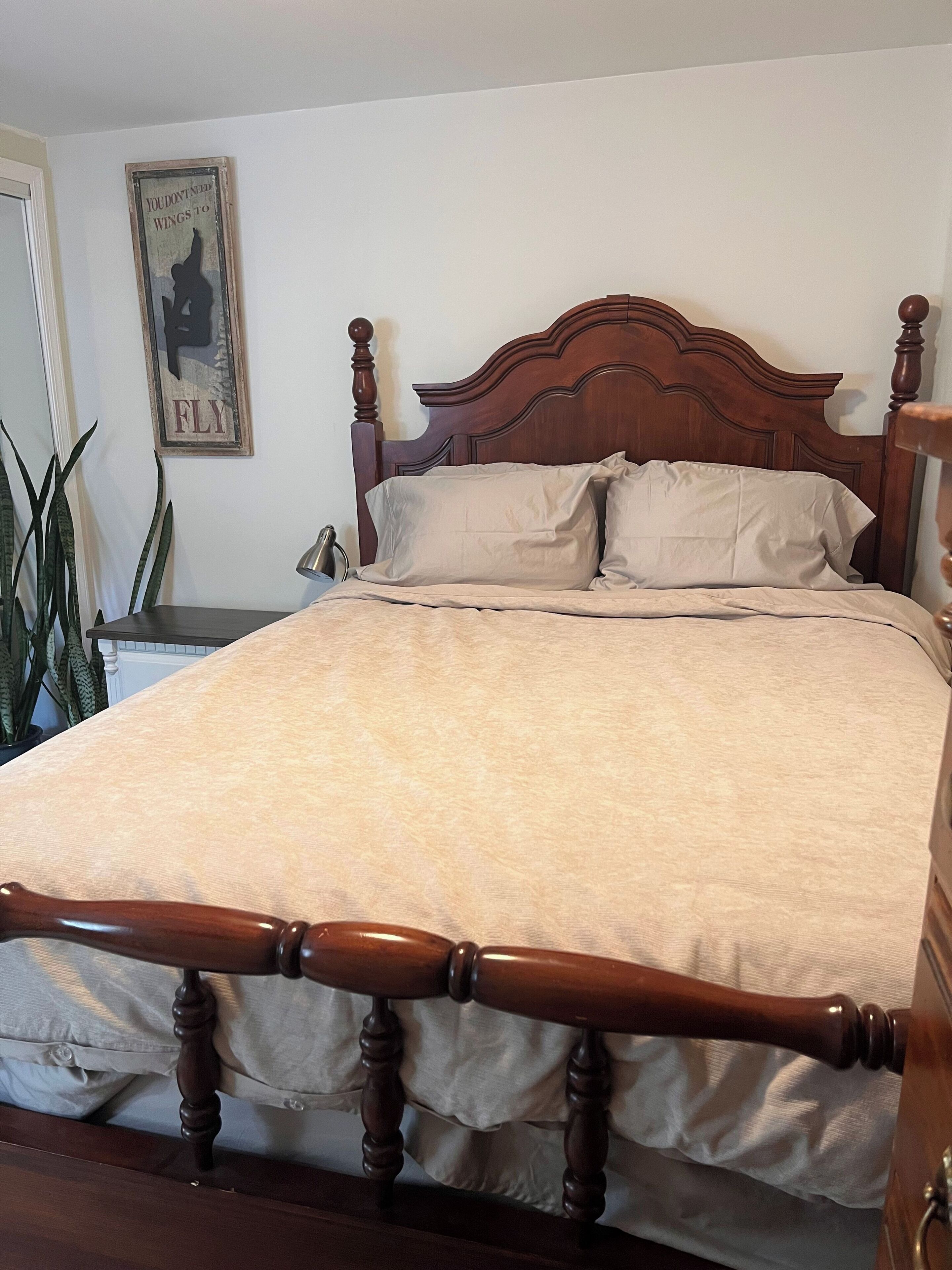 A bed with a wooden headboard, a nightstand with a lamp, and a poster on the wall.