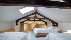 Ein Schlafzimmer mit schrägverdeckter Decke, Holzbalken und einem Oberlicht sowie zwei Betten.