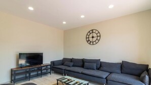 Ein modernes Wohnzimmer mit einem grauen Sofa, einem Fernseher auf einem Schrank, einem Couchtisch und einer Wanduhr.
