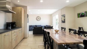 Eine moderne Küche mit Holzarbeitsplatte, ein Essbereich mit großem Tisch und Stühlen sowie ein Wohnbereich mit Sofa und einer Uhr an der Wand.