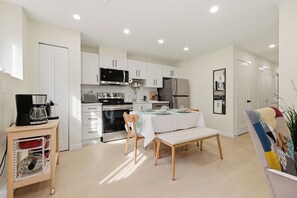 Une cuisine moderne avec des meubles blancs, un four à micro-ondes, une cuisinière et un réfrigérateur. On y trouve une table à manger avec des chaises et un banc.