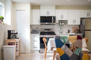 Una cocina moderna con armarios blancos, microondas, horno, cafetera y un comedor con mesa y sillas.