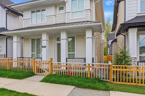 A residential building with a covered porch, a wooden fence, and a clear sky. - Luxurious 2BR Suite Near Langley Events Centre | King Bed | Fully Equipped (Langley Township)