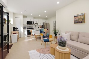 A modern living room with a sofa, a dining area with a table and chairs, and a kitchen with white cabinets and appliances. - Luxurious 2BR Suite Near Langley Events Centre | King Bed | Fully Equipped (Langley Township)