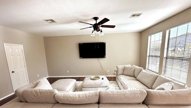 A living room with a sectional sofa, a ceiling fan, a mounted TV, and a window with blinds. - Spacious Luxe Retreat for family and groups Austin (Round Rock)