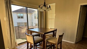 A dining area with a wooden table and four chairs, a chandelier, and a view of a neighboring house through large windows. - Spacious Luxe Retreat for family and groups Austin (Round Rock)