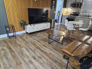 Un salon moderne doté d’un téléviseur à écran plat, d’un canapé en cuir marron, d’une table basse ronde et d’un coin repas avec des chaises blanches.