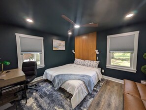 Una camera da letto con un letto, una scrivania, una sedia, una ventola a soffitto e finestre.